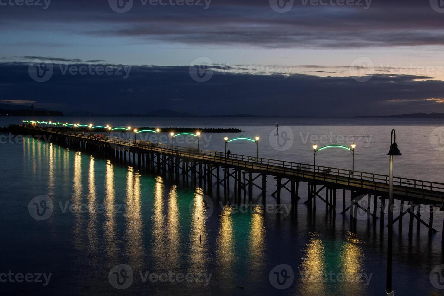 Evening lights illuminate the calm waters of a coastal pier during sunset in White Rock, BC photo
