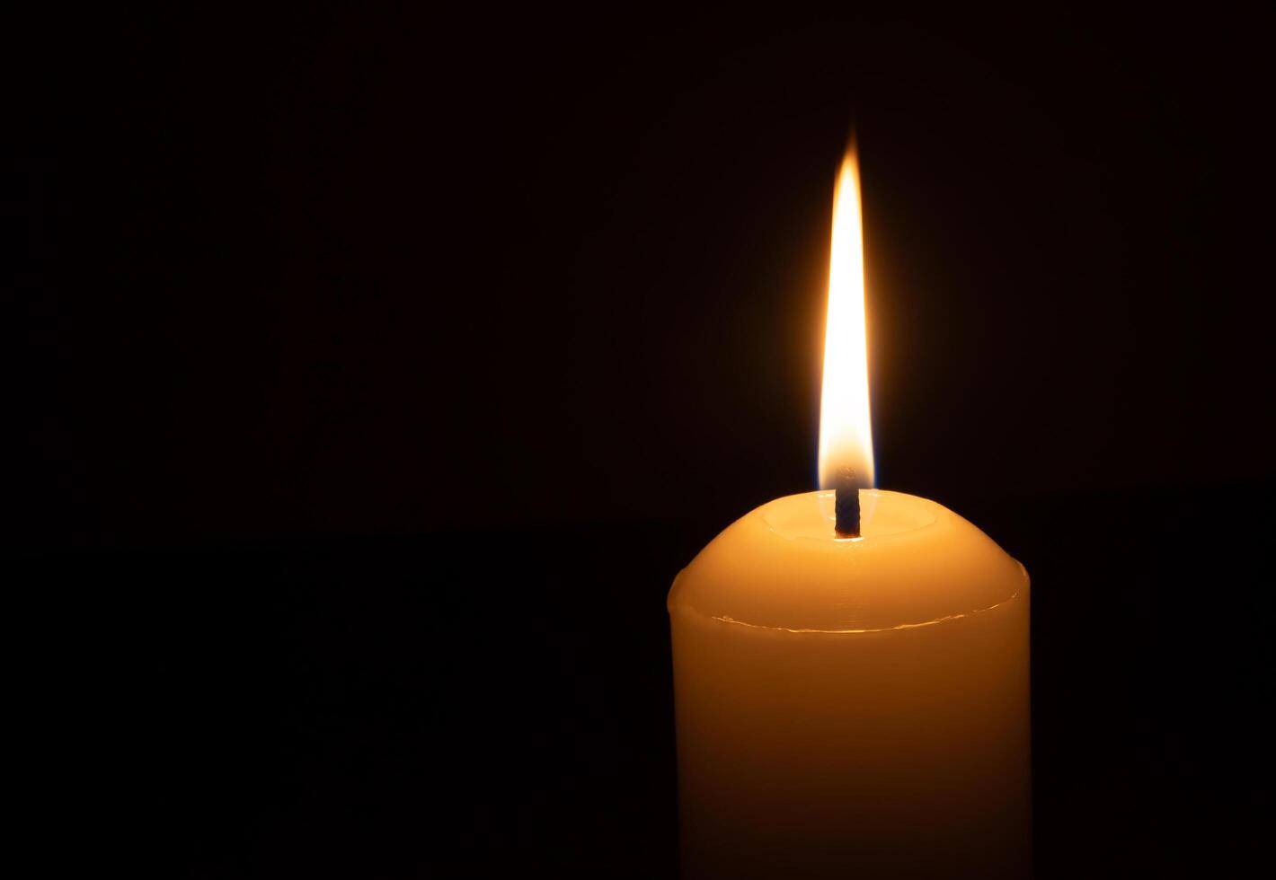 A burning candle flame or light glowing on a big white candle isolated on black or dark background on table in church for Christmas, funeral or memorial service photo