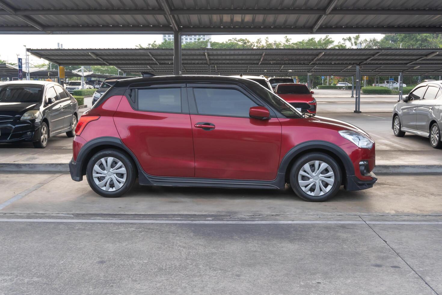 Right side view of mini or small red sports hatchback car with other cars parking in open area parking lot with roof of a department store photo
