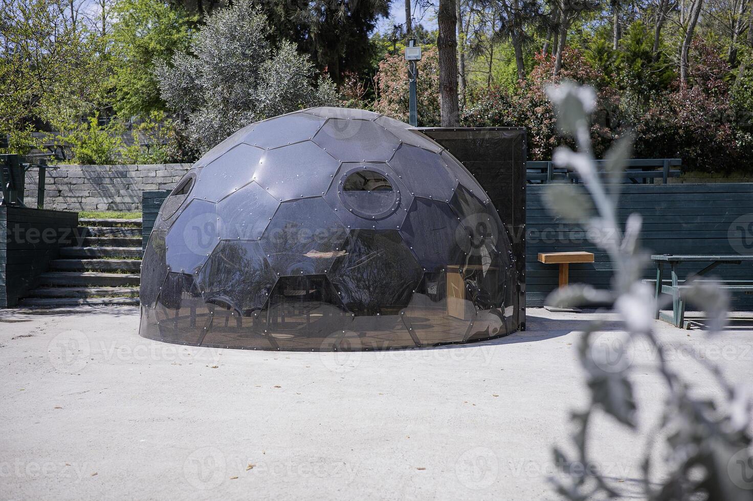 A black dome shaped building with a green plant in the background photo