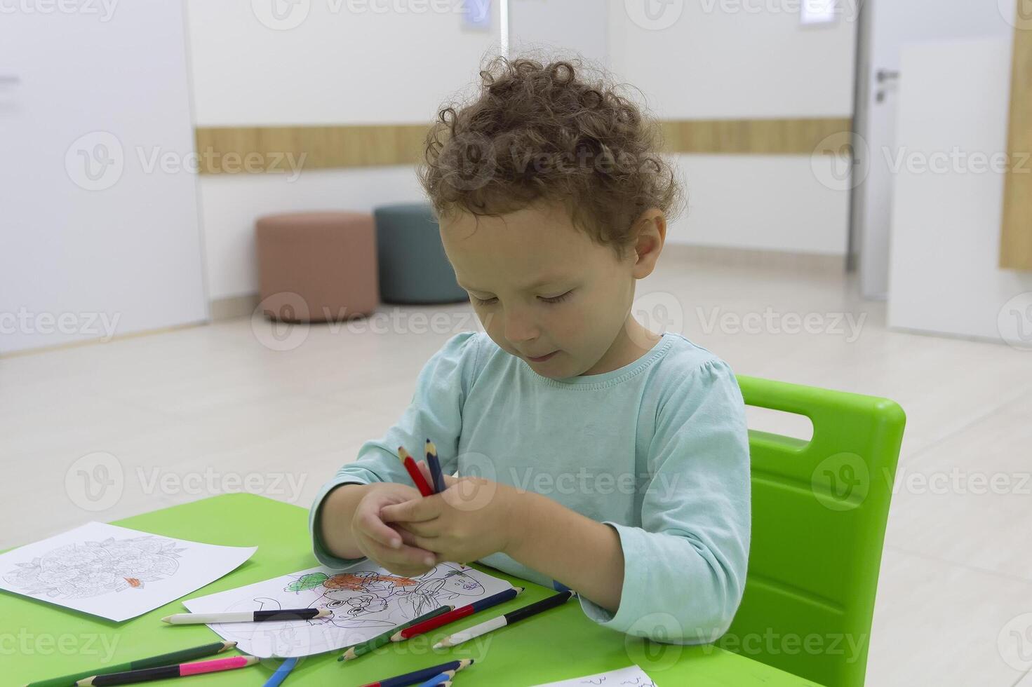 Curly child draws with pencils sitting at the table photo