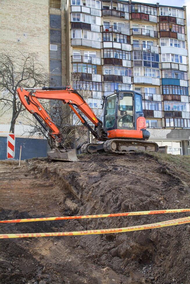 A bulldozer digging a foundation pit and operating at a construction site among residential buildings, behind a safety tape photo