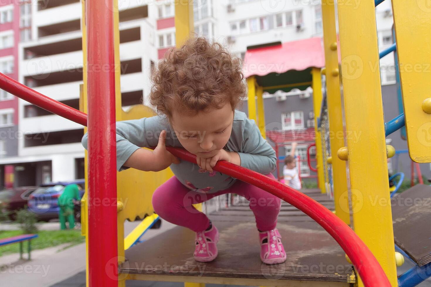 The curly child plays on the playground Near a multi-storey building photo