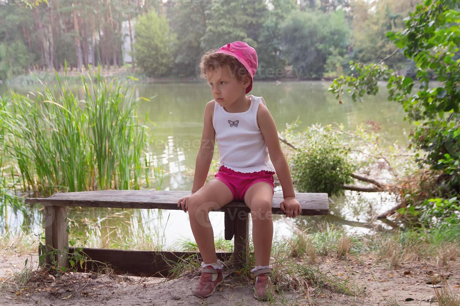 A child in panama hat sits on a bench on the lake photo