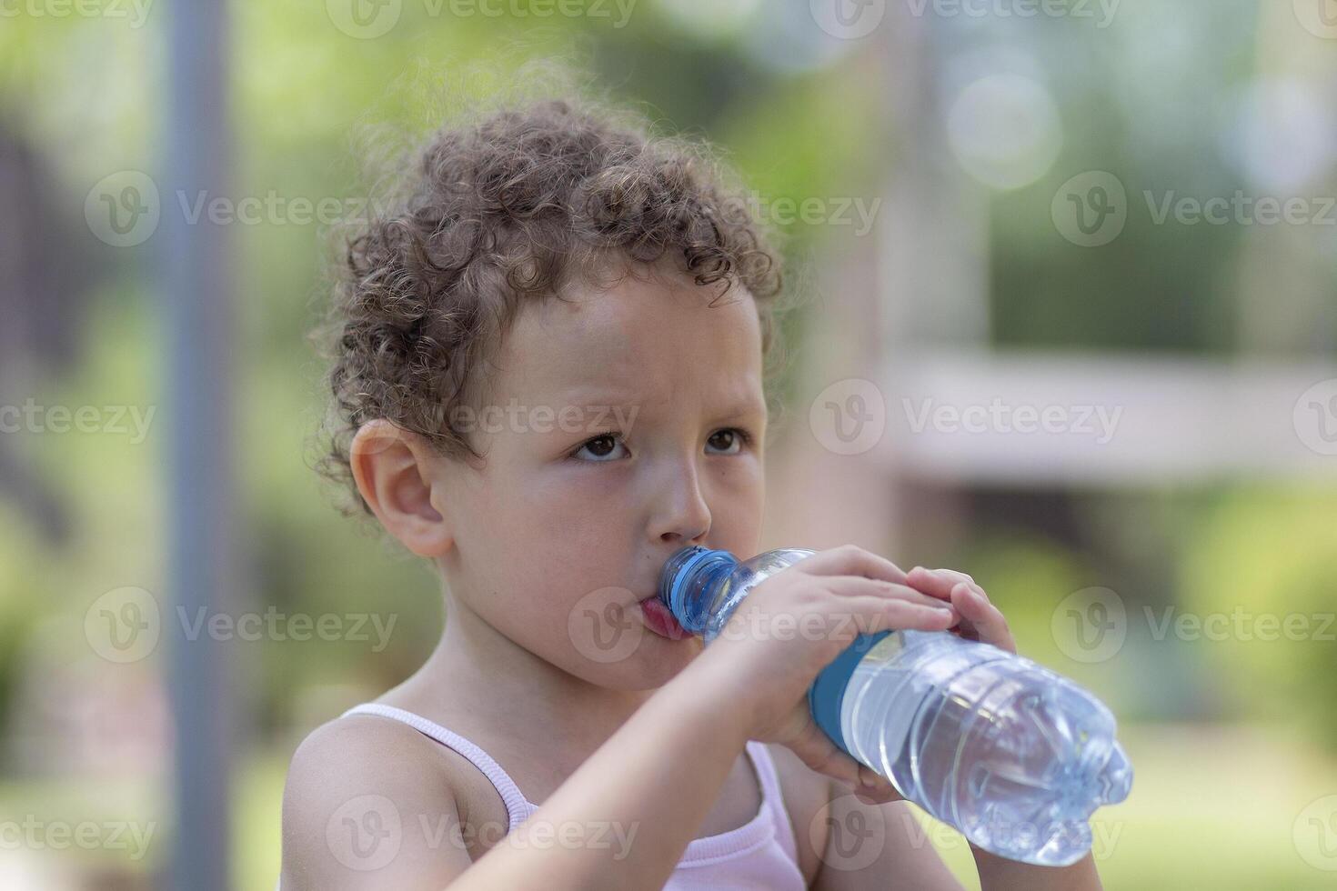 Curly child drinks water from a bottle in the summer photo