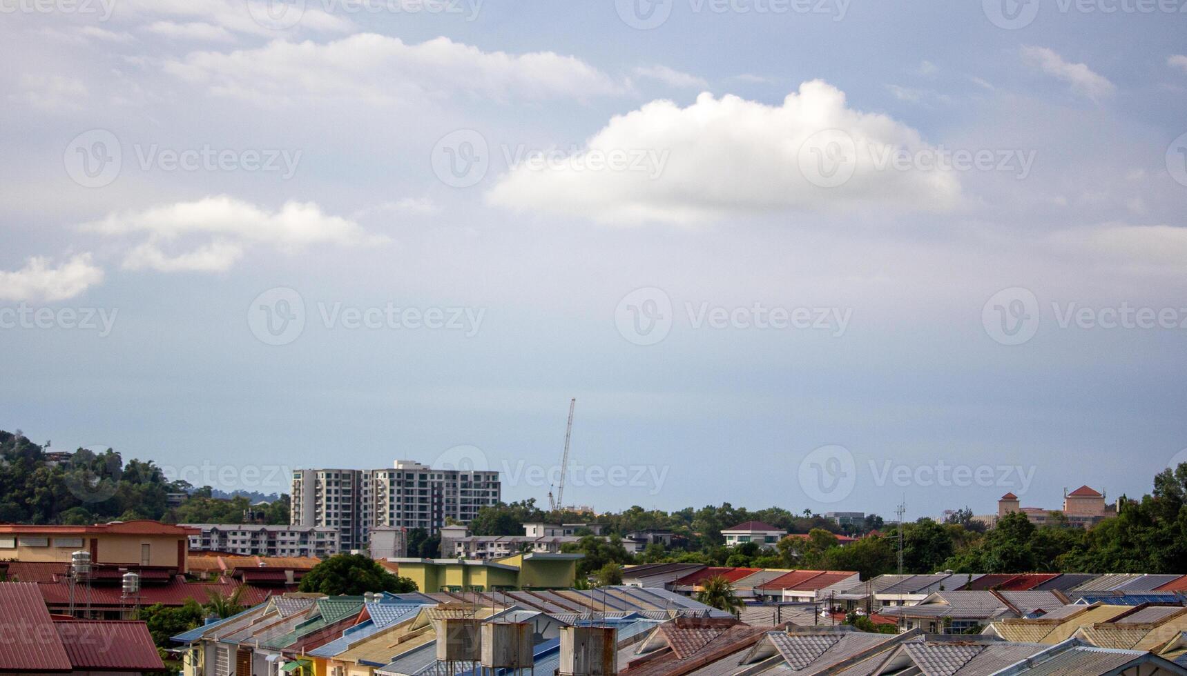 Urban residential rooftops beneath a clear blue sky with soft white clouds in peaceful daytime setting photo