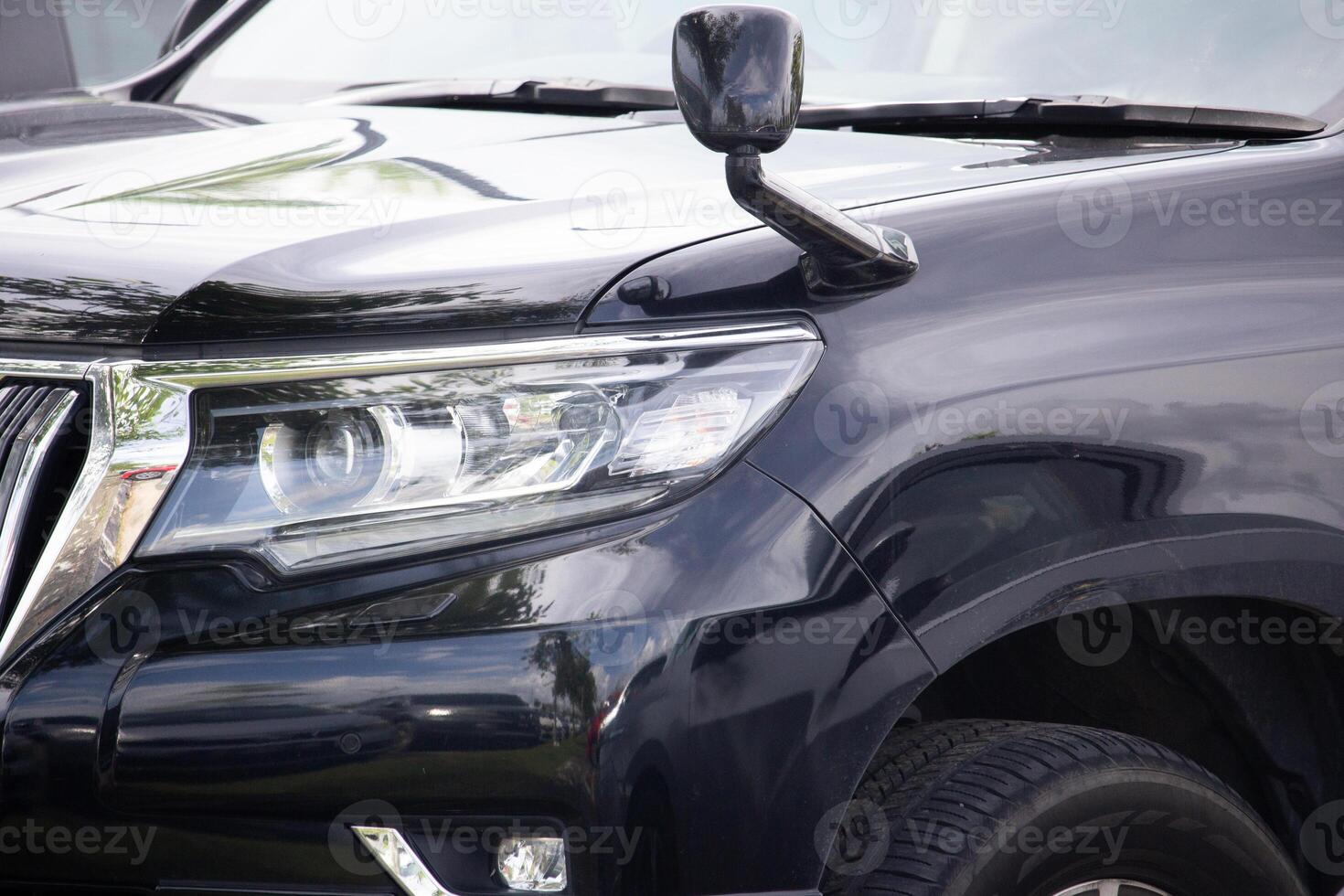 a modern black SUV front headlight, side mirror, and chrome grille in daylight photo
