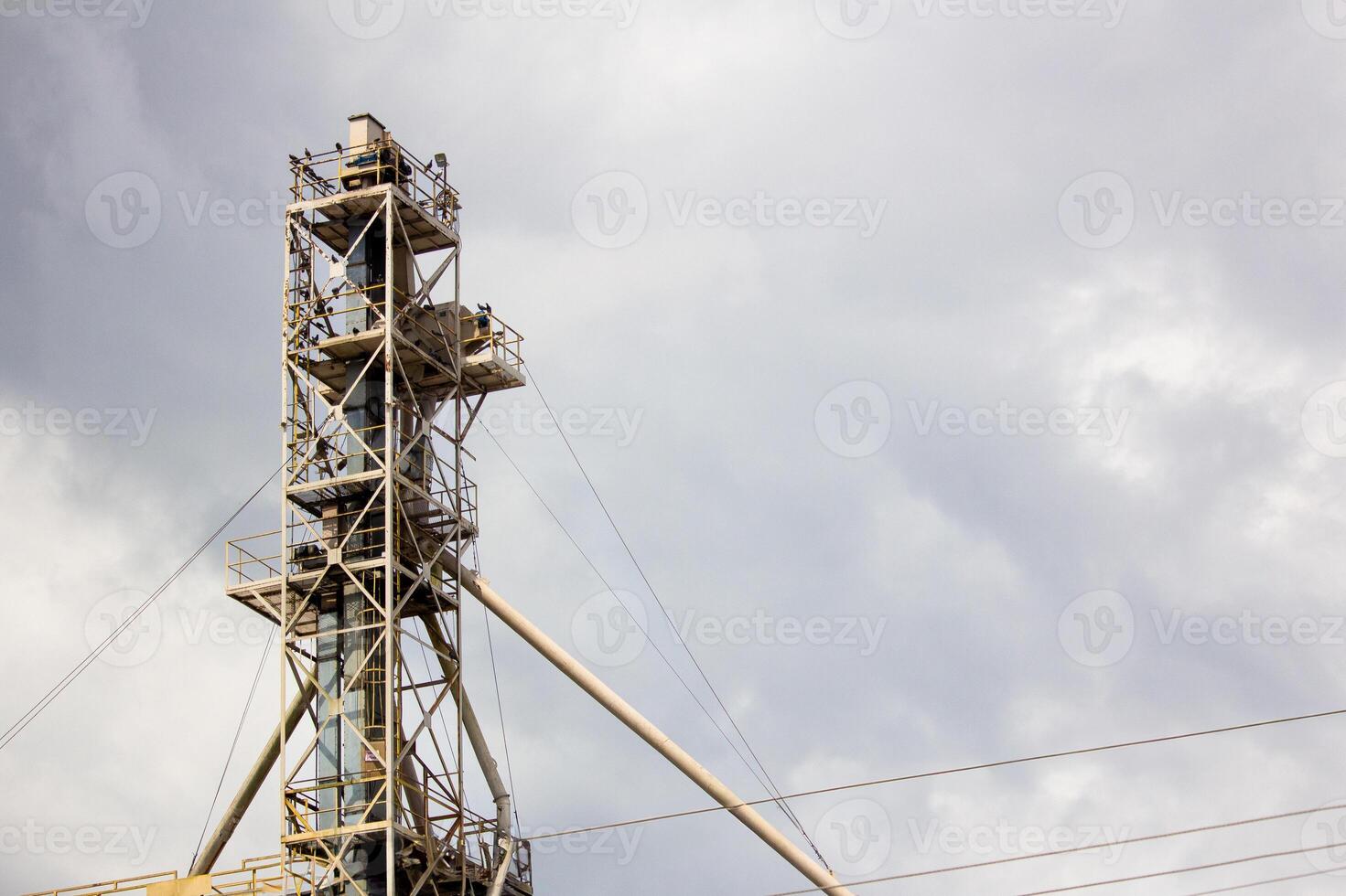 Tall industrial steel tower with yellow support beams and power lines under cloudy skies, ideal for industrial and construction themes photo