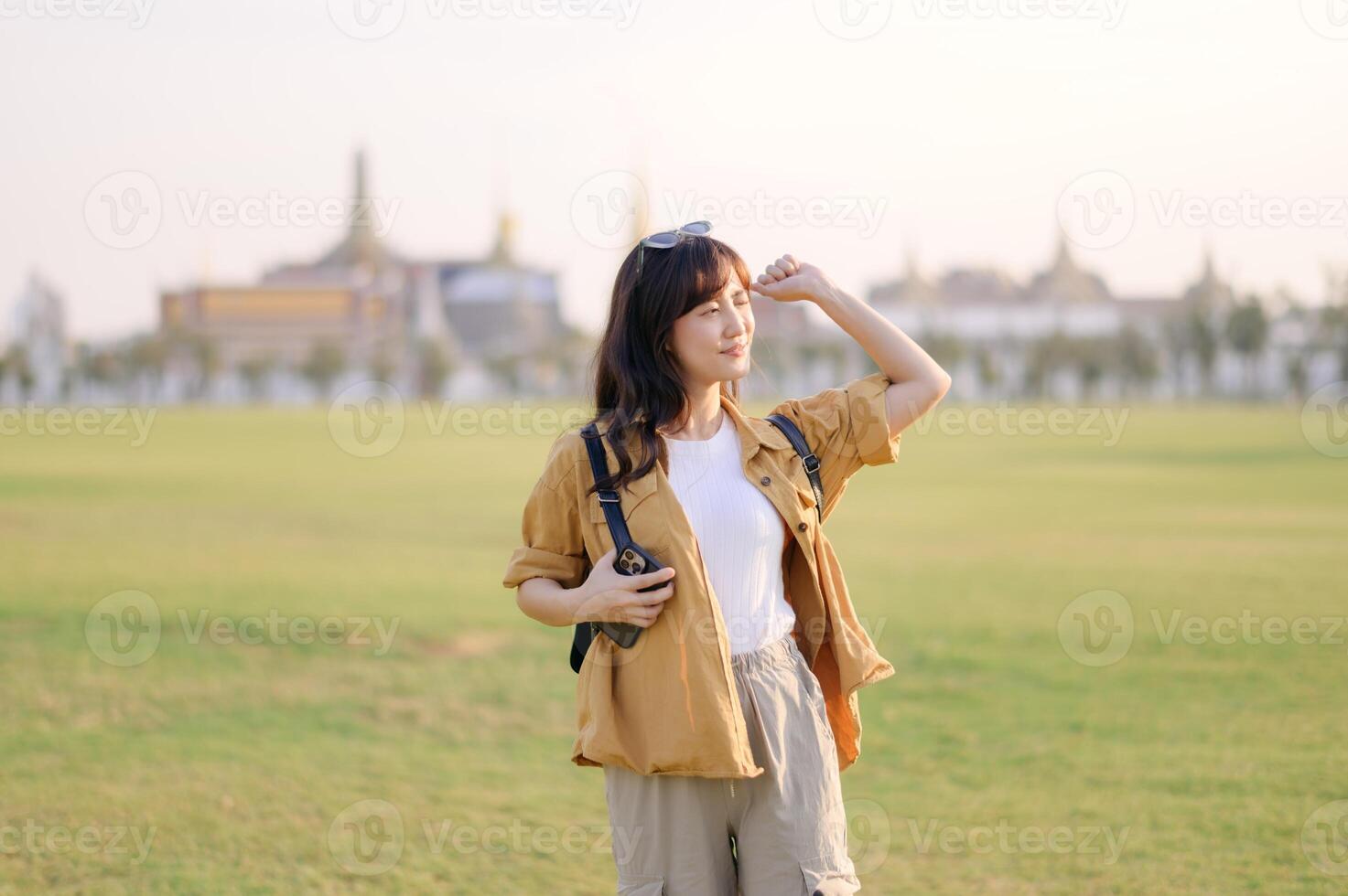 Asian woman in yellow jacket standing in grass with a building in background photo