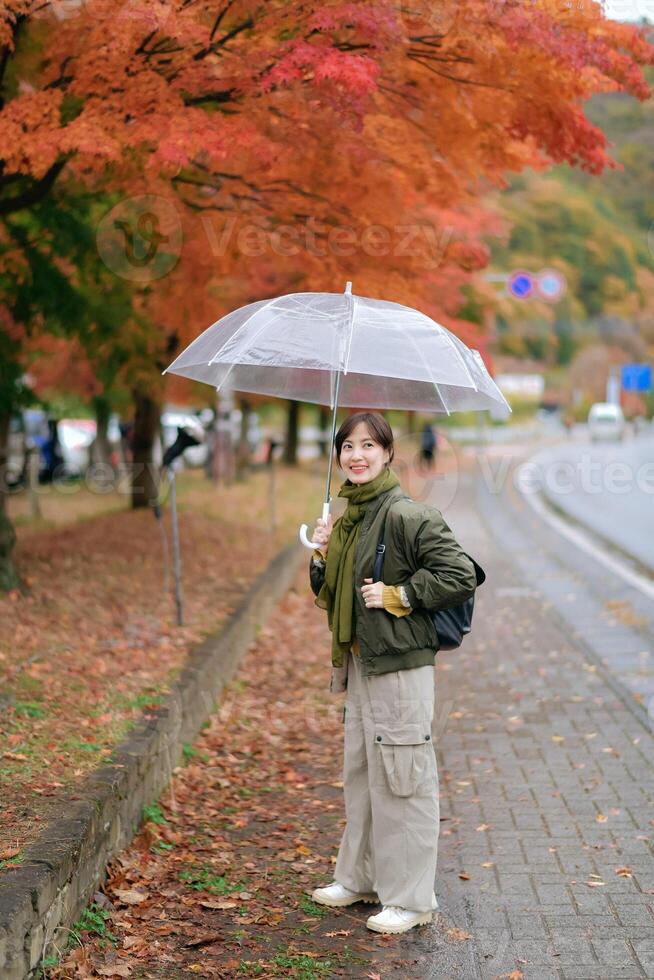 Asian woman with an umbrella enjoys the rain, surrounded by the colors of nature. A cheerful and happy portrait capturing the beauty of the season. photo