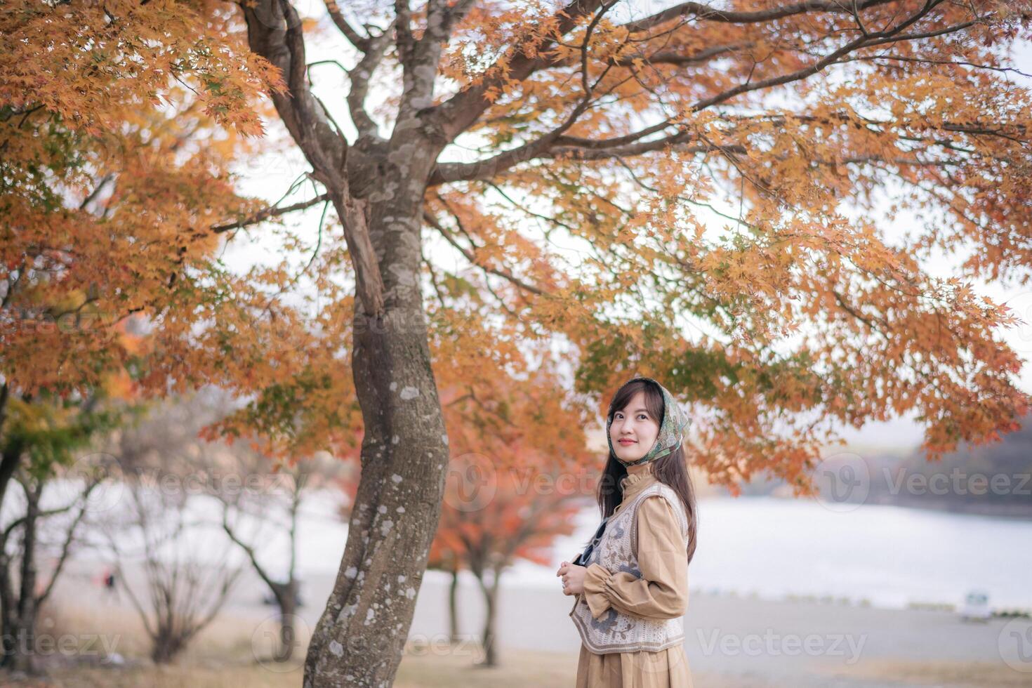 A woman standing under a tree in front of a lake photo