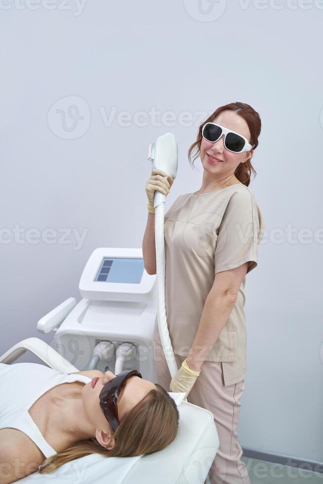 Female technician performing laser skin treatment on female adult client in modern clinic environment. photo