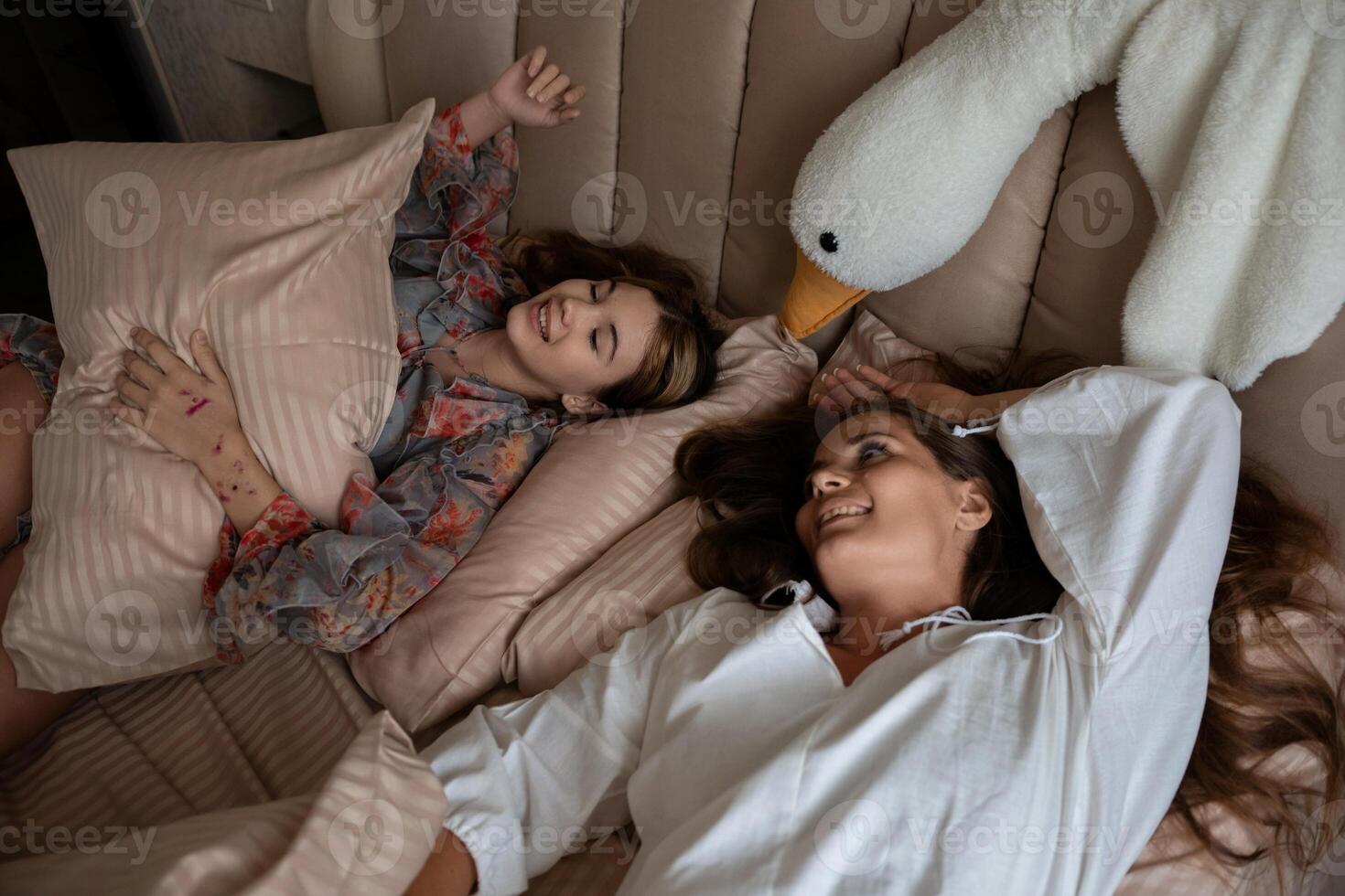 Swan Pillow Women Bedroom. Two women playfully relax in bed with a swan-shaped pillow intimate moment captured indoors. photo