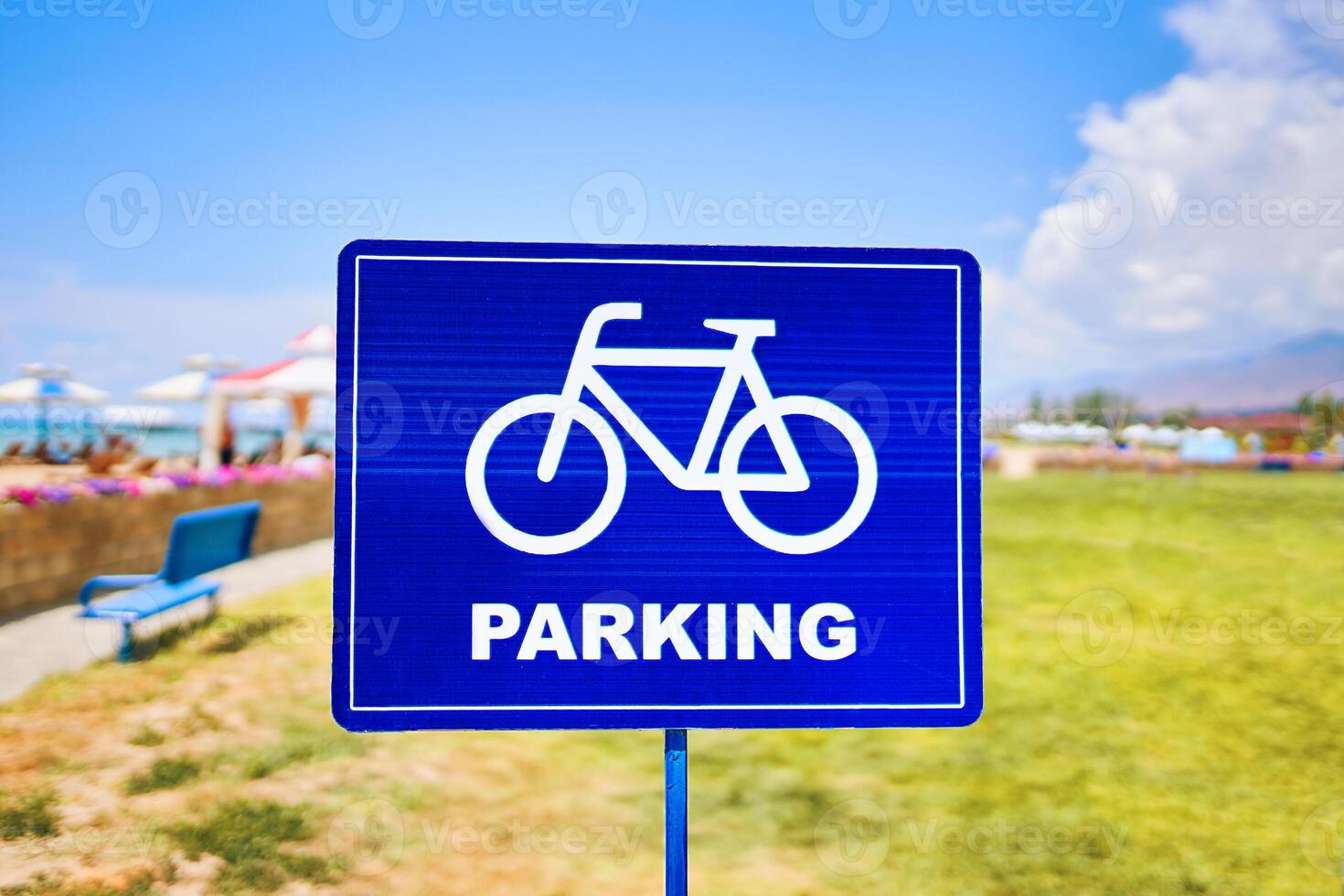 A vibrant blue traffic sign featuring a silhouette of a bicycle wheel parked against a sky backdrop with fluffy clouds. The font stands out against the natural landscape photo