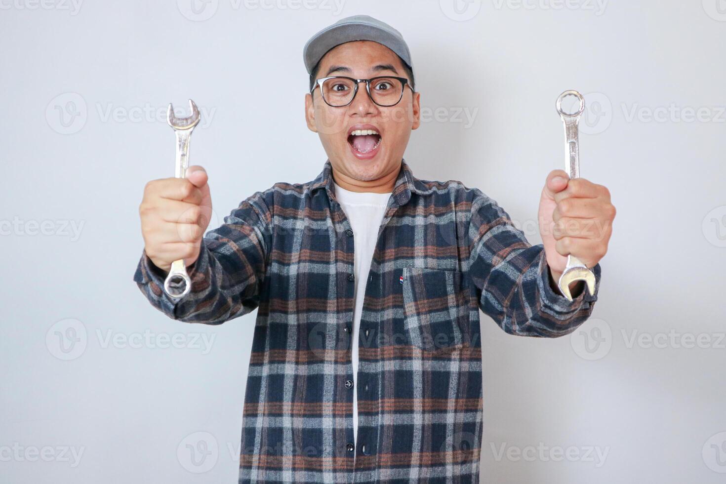 Indian happy auto mechanic in blue suit and cap holding spanner tool with laptop or check list or writing pad or using smartphone photo
