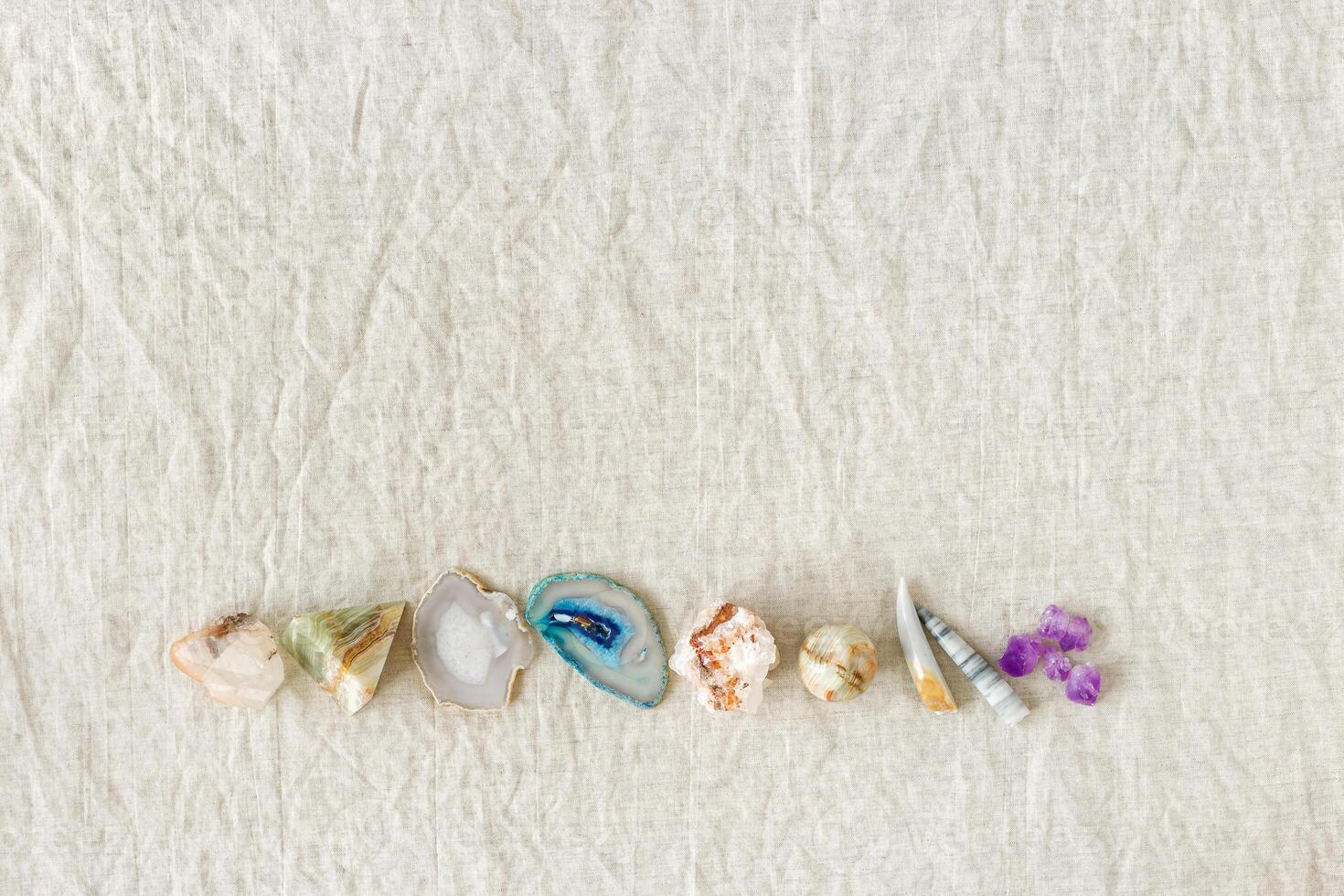 Row of crystals on table, healing minerals agate, quartz, amethyst, onyx, semiprecious gem. Stones for stone therapy, lithotherapy, rocks for ritual. Top view, flat lay with daylight photo