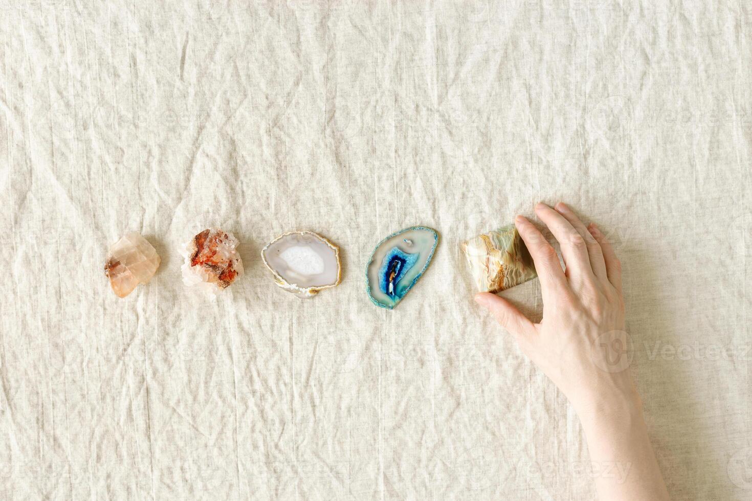 Row of crystals on table, woman hand holding onyx pyramid, healing minerals agate, quartz, amethyst, onyx. Stones for stone therapy, lithotherapy, rock for ritual. Top view, flat lay photo