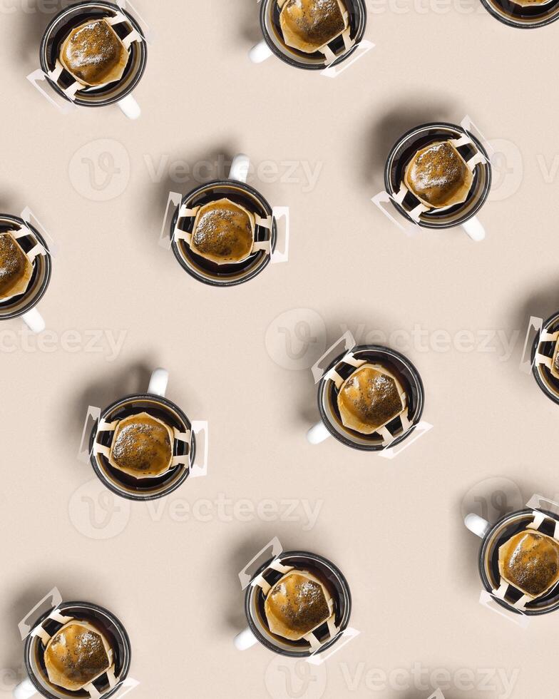 Pattern with black coffee cups, drip coffee bag with ground coffee for brewing in cup, paper bag drip coffee filter, beige background, top view, minimal trend flat lay photo