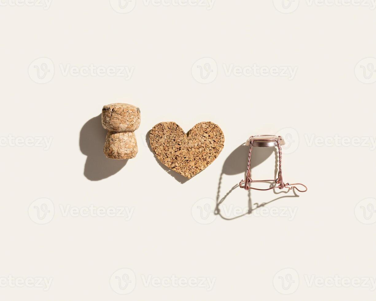 Champagne cork and heart on beige background with hard light, shadows at sunlight. Summer drinks concept, bottle cap from sparkling wine and pink metal wire muselet, minimal flat lay. photo