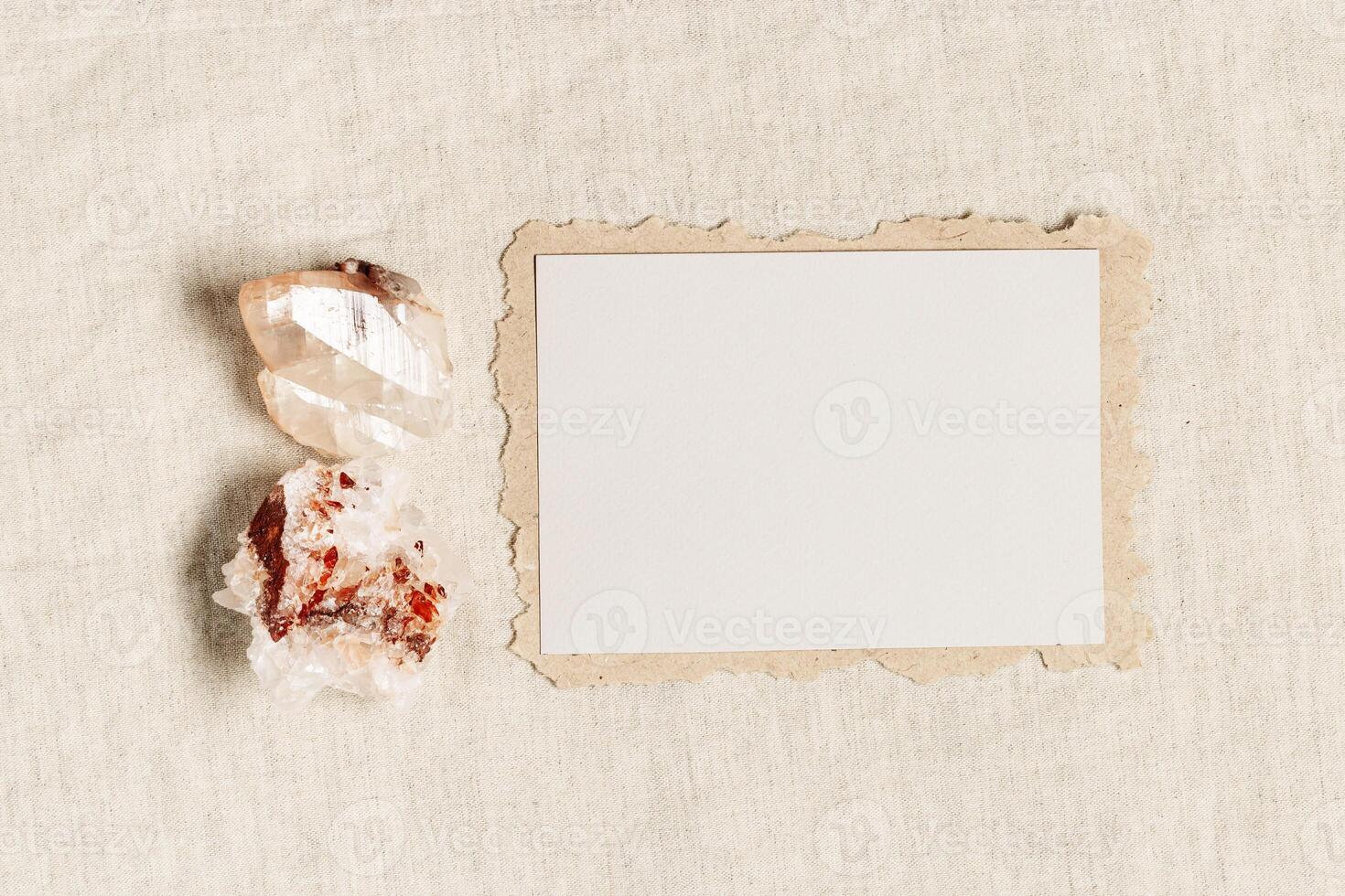 Empty Invitation card, blank card with protection crystal, healing stone quartz on fabric background tablecloth. Torn craft paper with copy space for text, top view mock up paper postcard photo