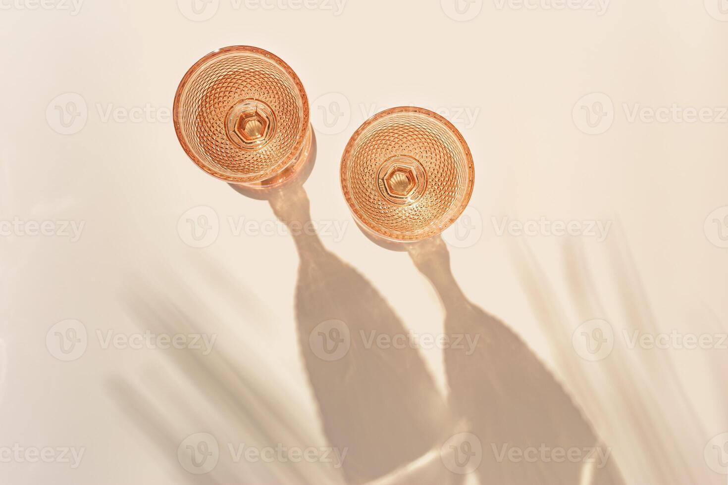 Two wine glasses from peach color glass with palm leaf shadows from sun, trendy goblets style wine glasses with white wine on beige background. Pastel colors, monochrome, top view glassware photo
