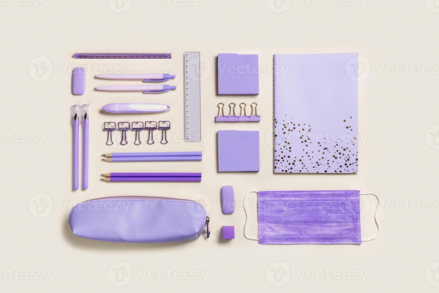 School stationery flat lay violet color. Back to school new normal concept, notebook, note, pen, pencil, clips, medical mask on beige background. Office equipment pattern, top view photo