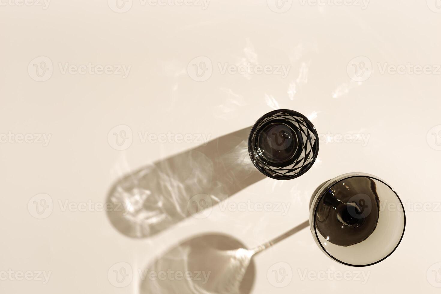 Champagne, wine, water glasses from tinted gray glass on beige table background with beautiful shadow and caustic from sunlight. Summer drinks concept. Vintage colored glassware photo