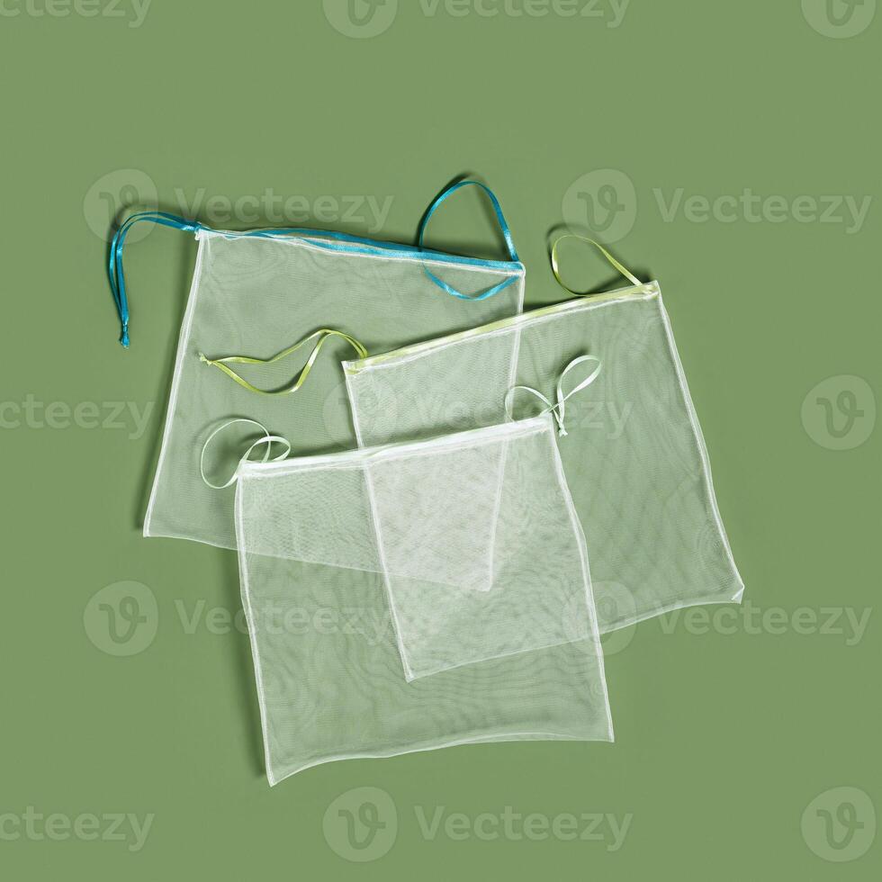 Reusable produce bags, diy fom organza textile, reusable packaging for fruits and vegetables, mesh bag with ties, eco friendly and zero waste concept, flat lay on olive color background photo