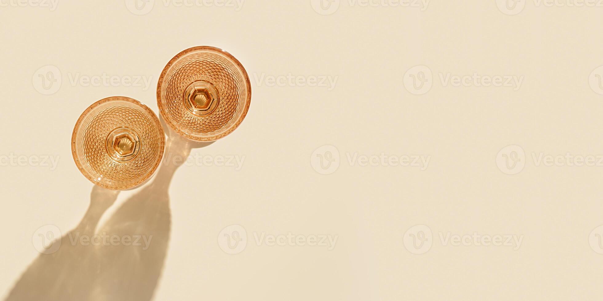 Two wine glasses from pale pink colored glass with hard shadows from sunlight, creative summer drink minimal concept, white wine glasses in goblets style on peach color background, copyspace photo