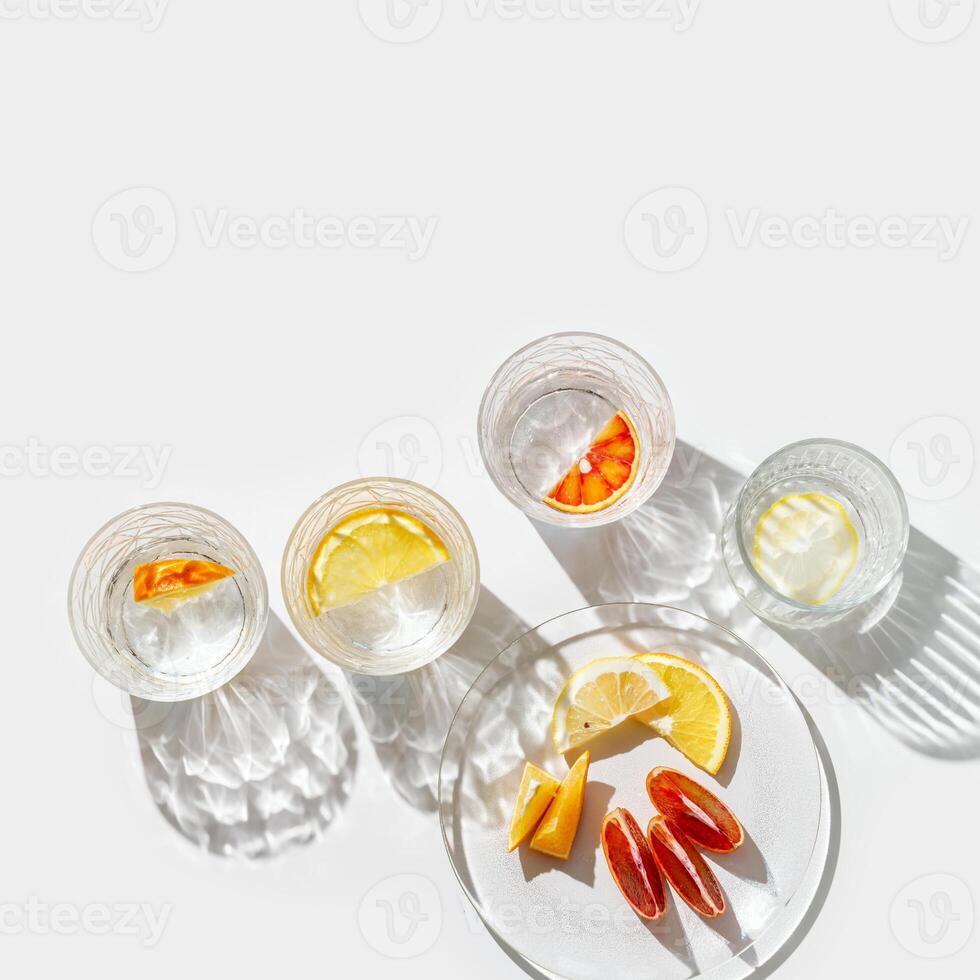 Citrus Infused Water in clear Glasses and plate, artistic light reflections and shadows in natural sunlight. Summer drink concept, minimal pattern, flavored water with yellow red slices of fruit photo
