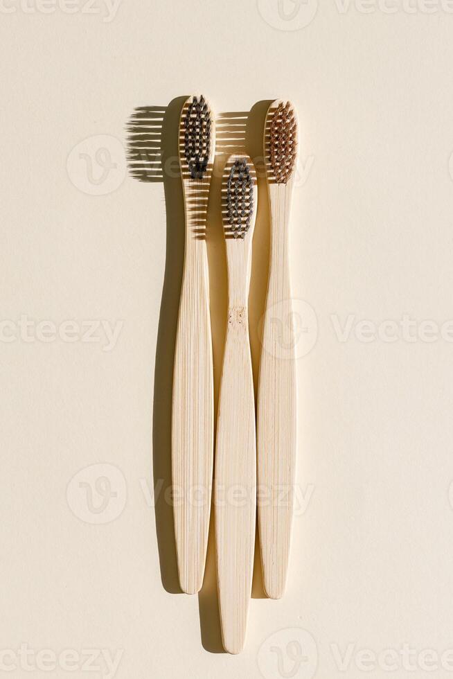 Eco-friendly Bamboo toothbrushes with white bristles at sunlight with dark shadows on beige background. Sustainable living concepts, minimal style aesthetic photo, top view set wooden brushes photo