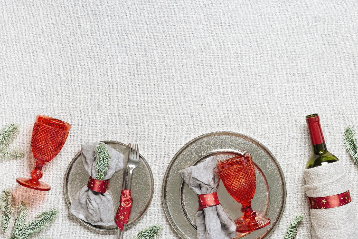 Tableware for Christmas or Xmas festive dinner, linen napkin on plate, knife, fork, red wine glass, bottle of wine on rustic tablecloth, New Year holiday cutlery, red decor, above view photo