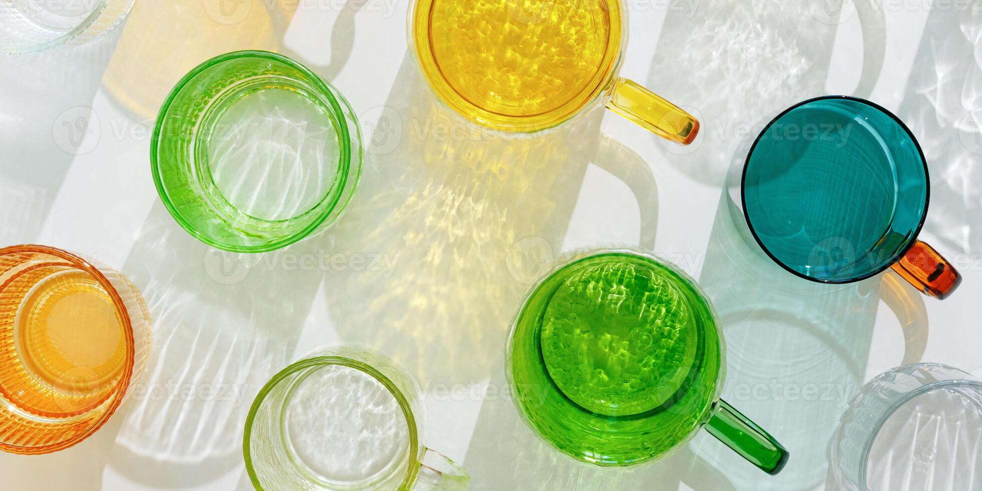 Colored shiny drink Glasses still life banner with shadow and sunlight reflections on white, minimal aesthetic top view summer photo, refraction at glass cups with sun glare, creative pattern photo