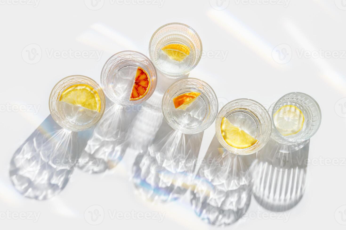 Citrus Infused Water in clear Glasses casting artistic light rainbow reflections and shadows at sunlight. Summer drink concept, minimal style pattern, flavored water with tasty slices of fruit photo