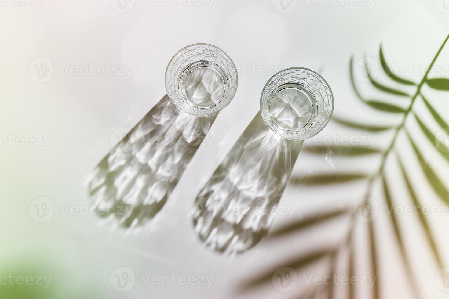 Water Glasses with palm leaf Shadows and sunlight Reflection on white background, colored photo minimal style, aesthetic top view summer still life, refraction throug crystal shine cups, caustic