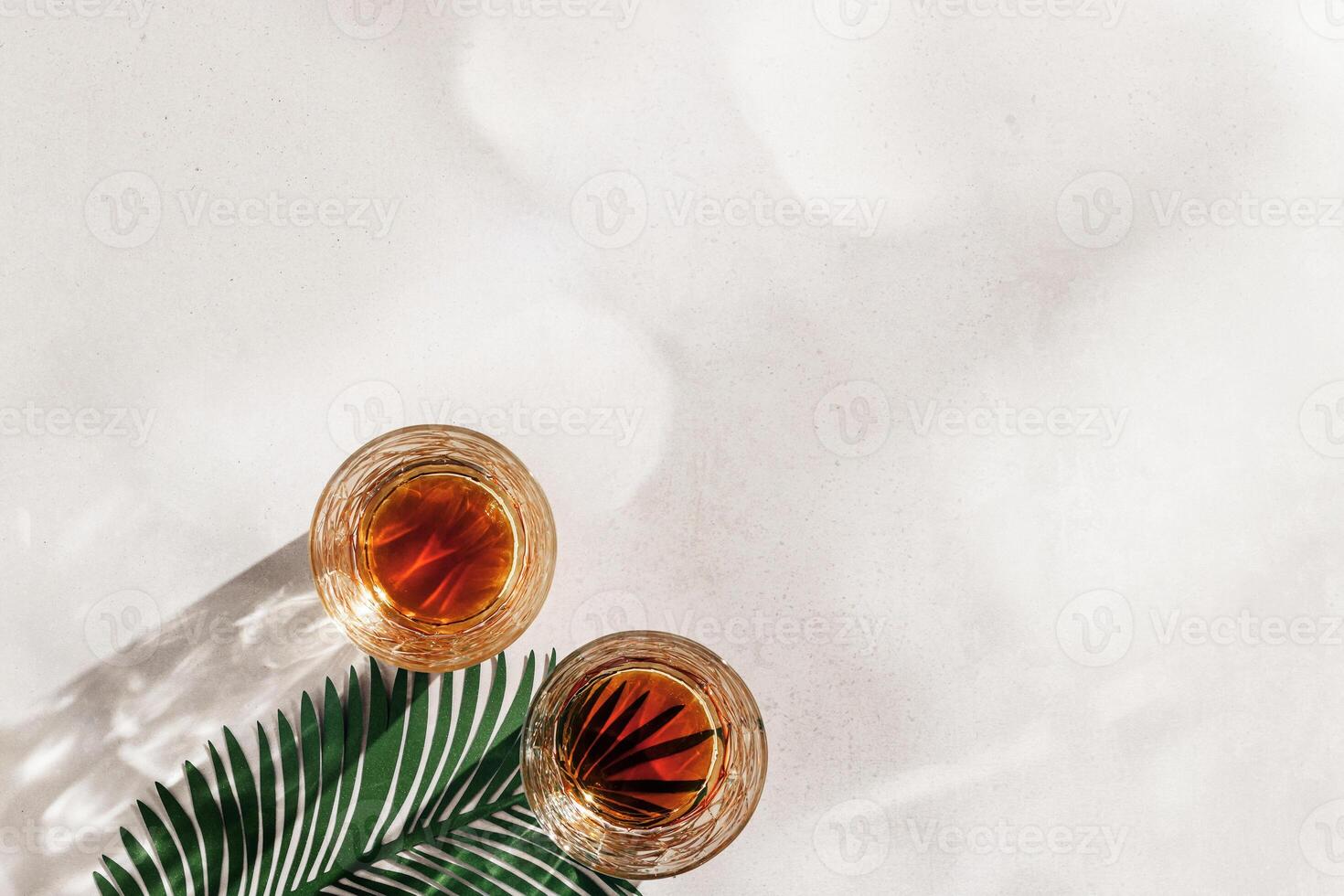 Whiskey Glasses with Shadow and sunlight Reflection on beige background, glass strong alcohol, palm leaf decor, aesthetic top view summer still life, refraction at crystal shine cups, caustics photo