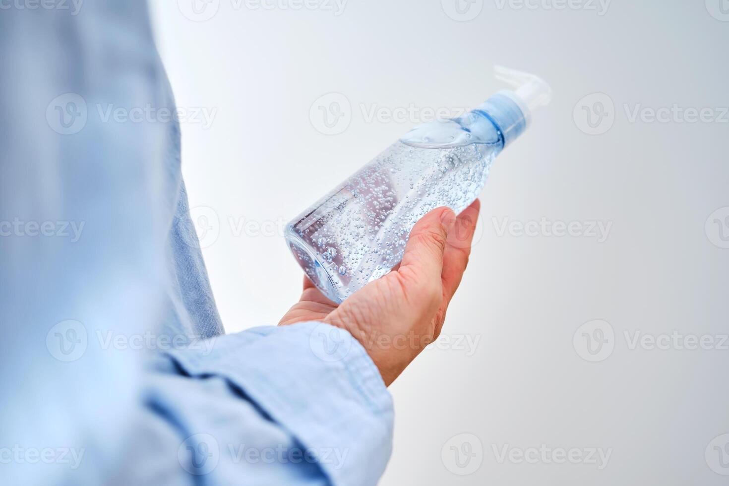 An unrecognizable person in blue clothes holds a bottle of hyaluronic micellar gel for washing. photo