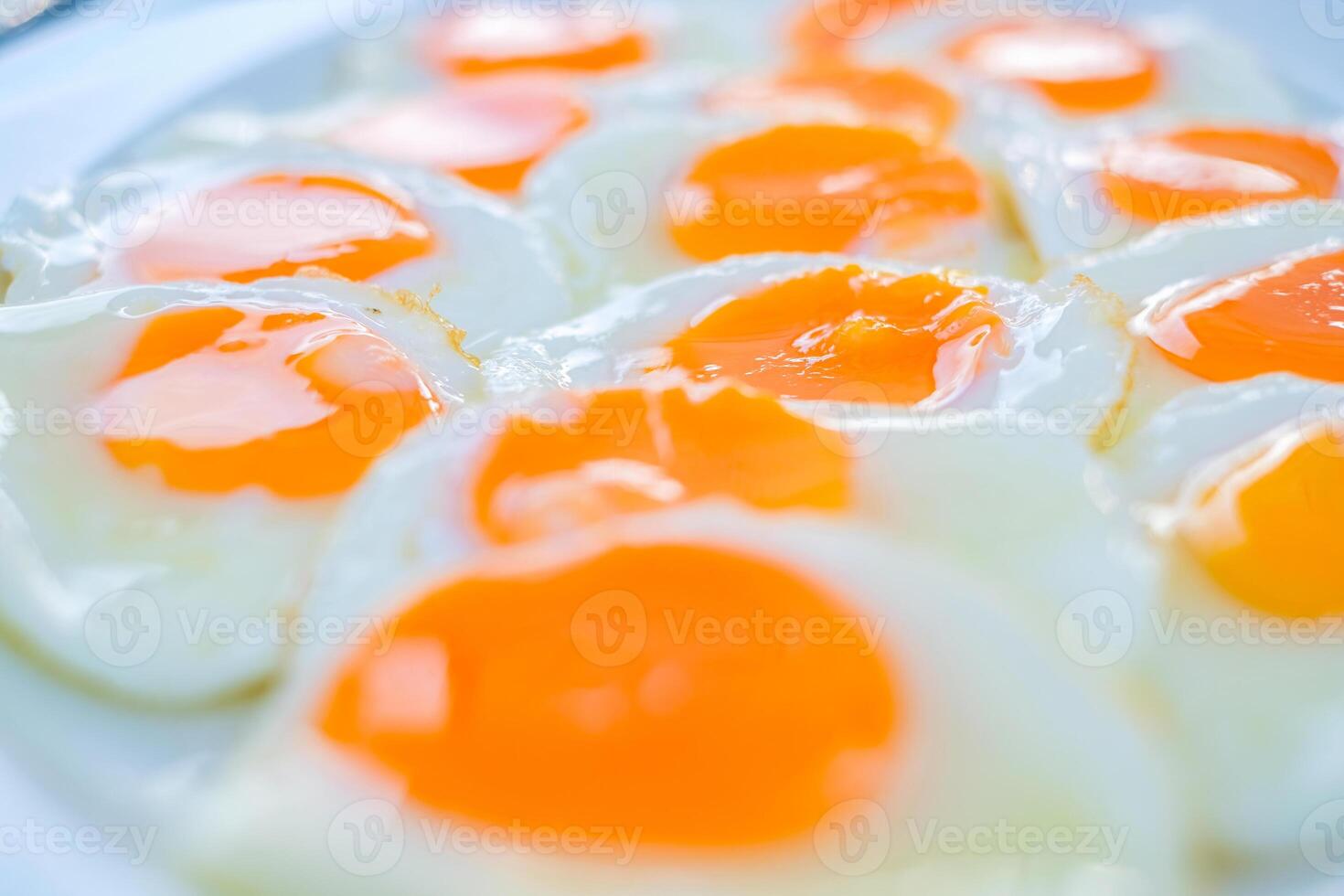 Close up of multiple sunny-side-up eggs with vibrant orange yolks and glossy whites, freshly cooked and arranged on a white plate, perfect for breakfast or food related concepts photo