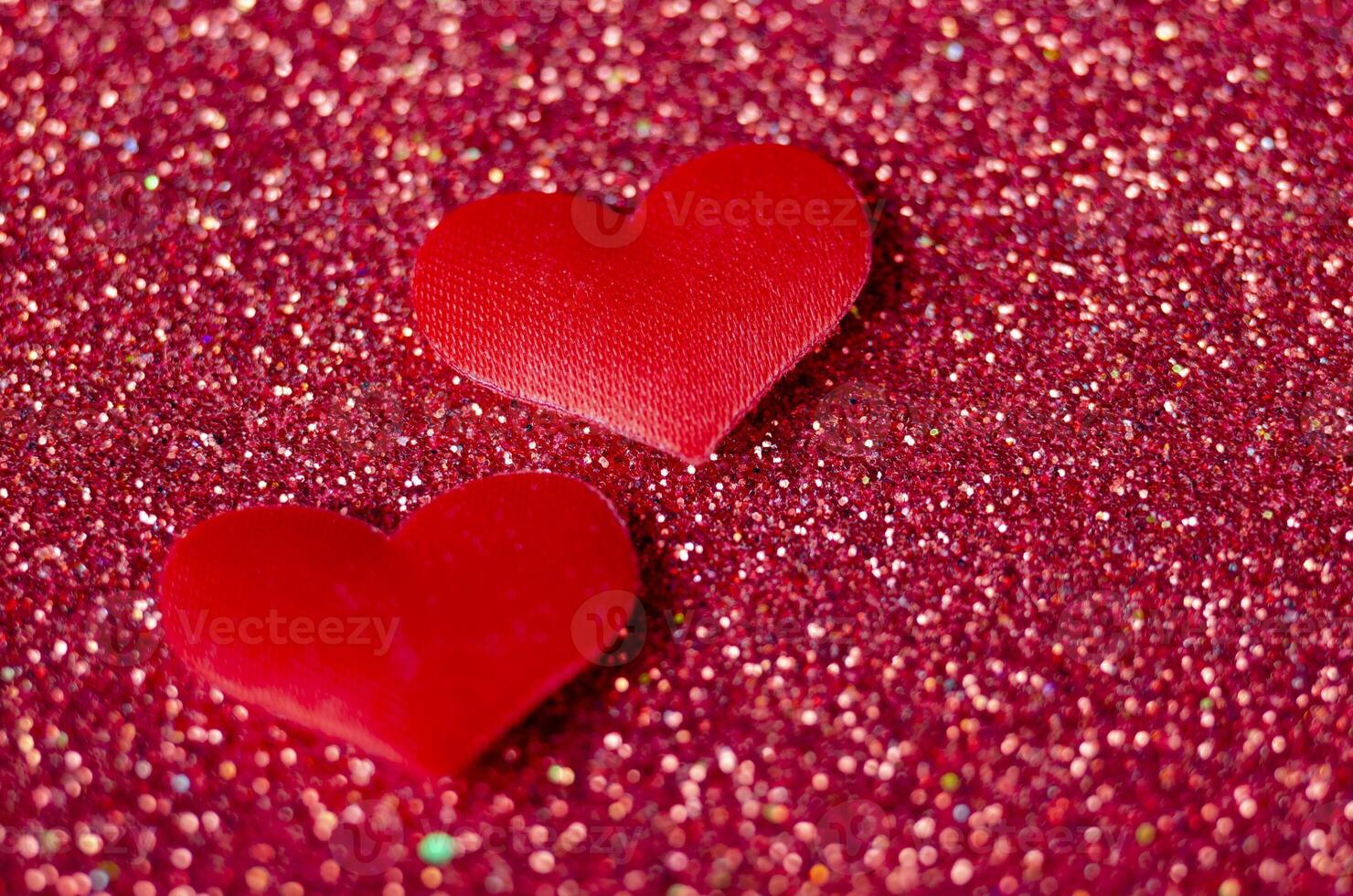 Side view of two tiny red hearts on sparkle red background with customizable space for text or wishes photo