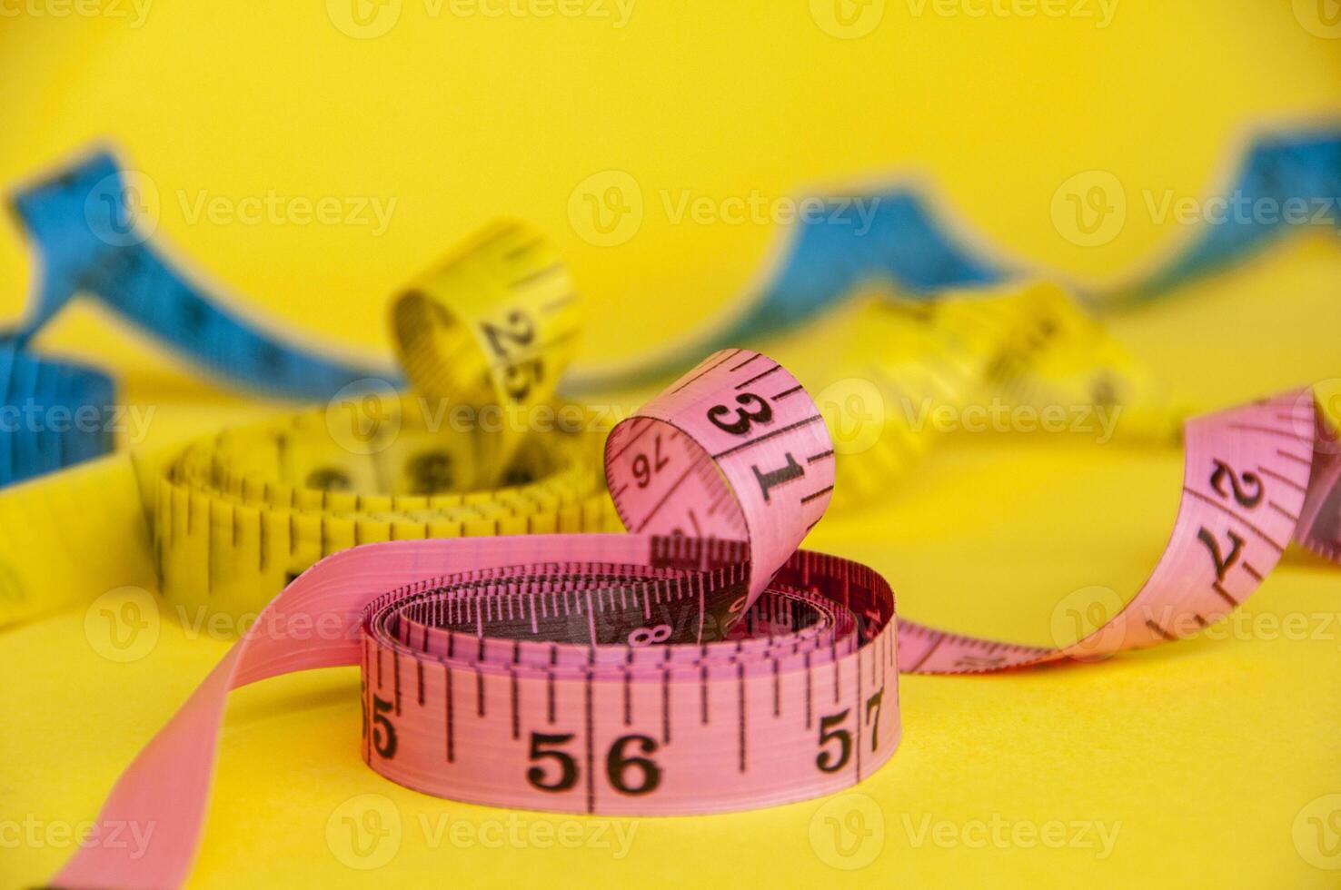 Pink, yellow and blue tape measure on yellow background with customizable space for text. Dieting concept photo