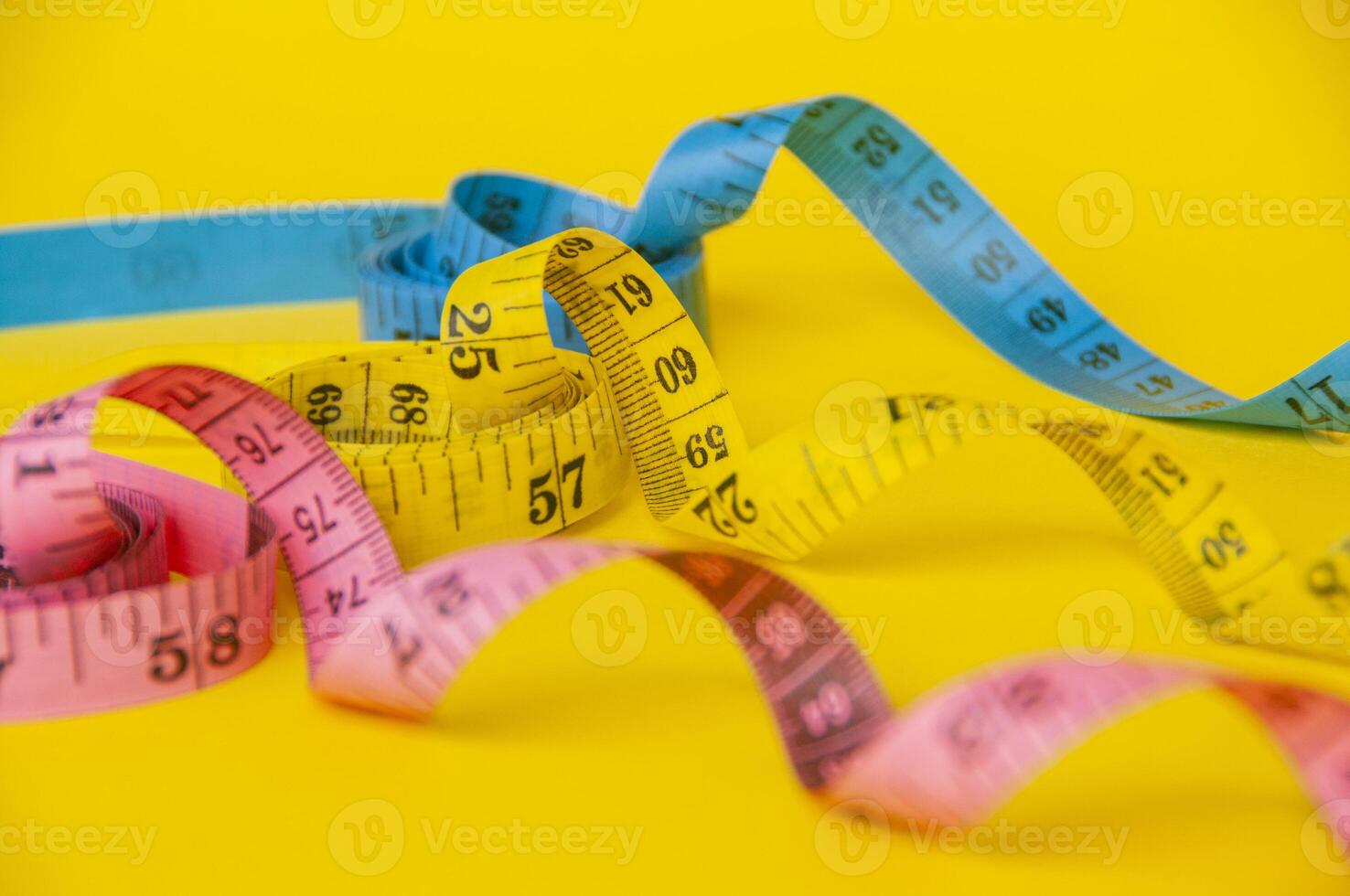 Pink, yellow and blue tape measure on yellow background with customizable space for text. Dieting concept and copy space photo