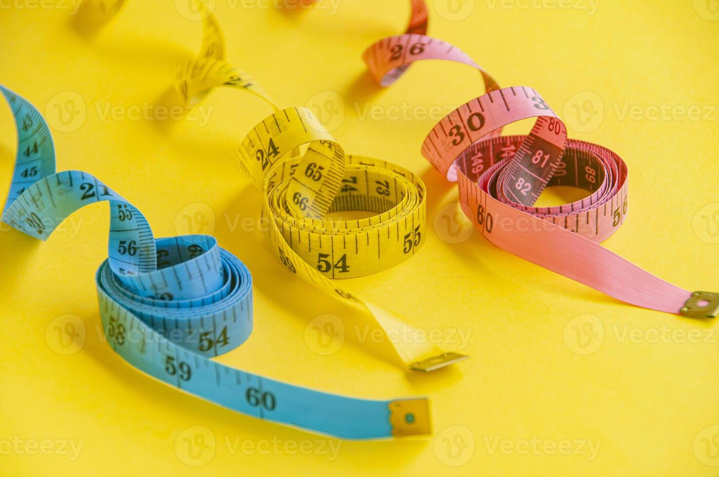 Precision and creativity symbolized by a blue, yellow and pink tape measure on yellow canvas. Dieting concept photo