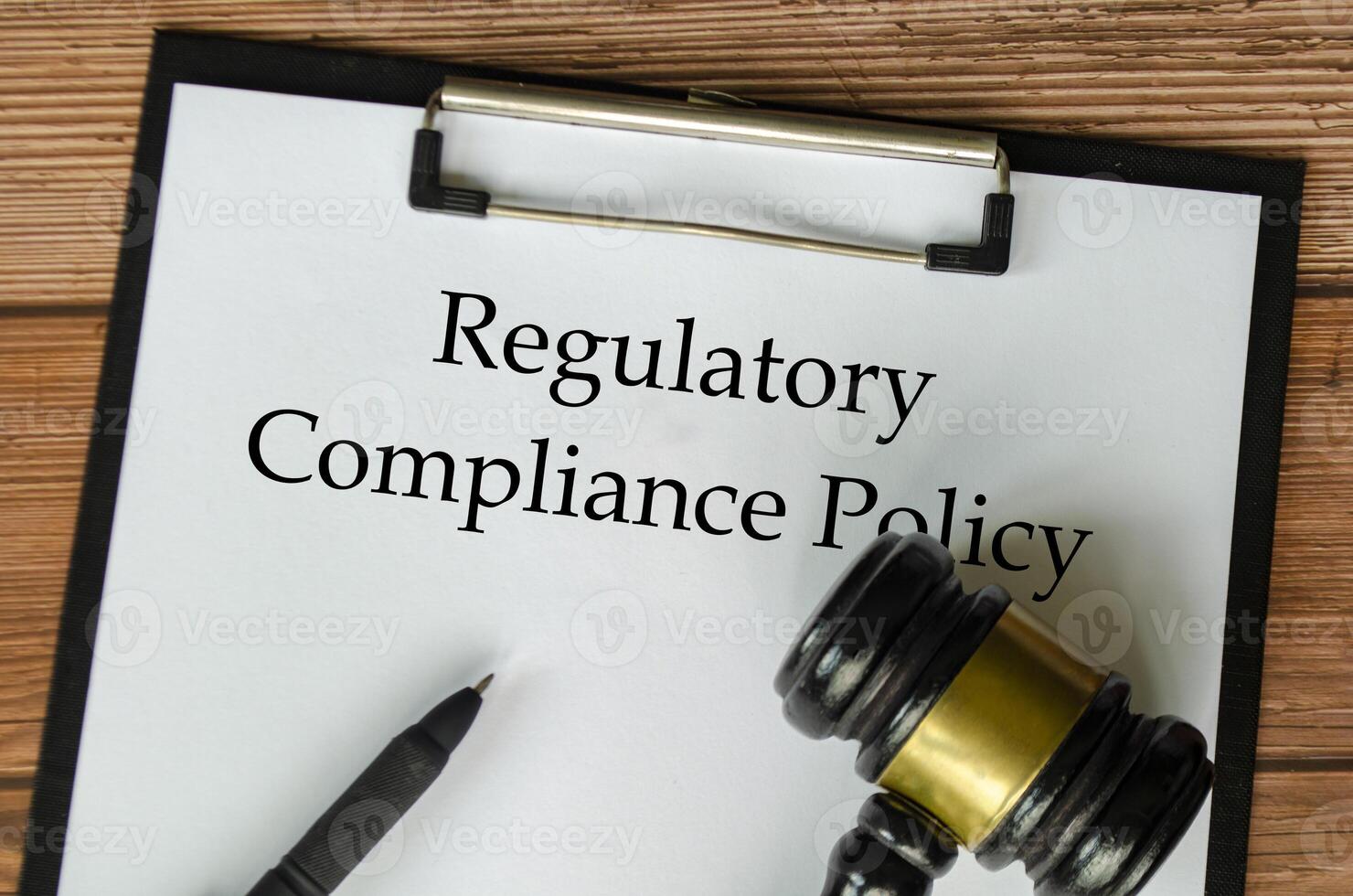 Regulatory Compliance Policy text on clipboard surrounding with magnifying glass and gavel. Compliance concept photo