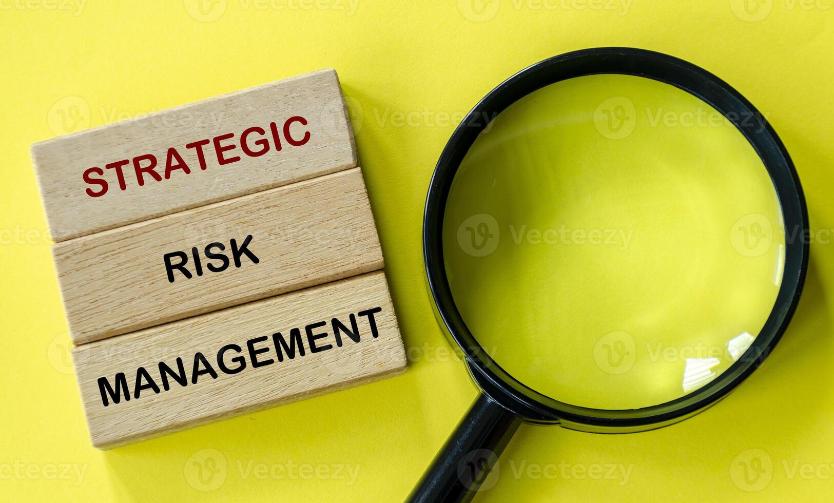 Strategic Risk Management text on wooden blocks with magnifying glass on yellow background. photo