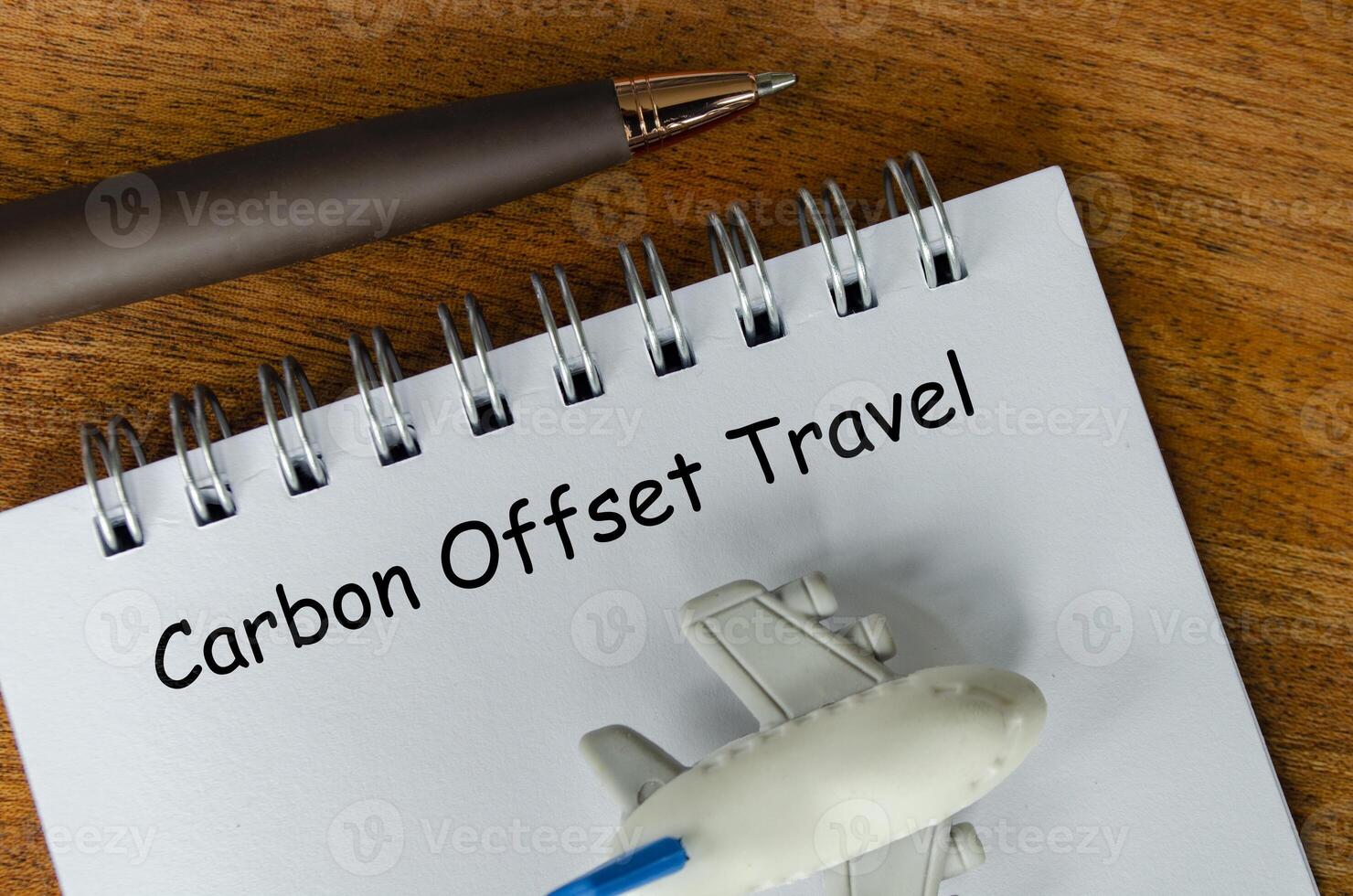 Top view of Carbon Offset Travel text on white notepad with small airplane and pen background. Environmental awareness photo