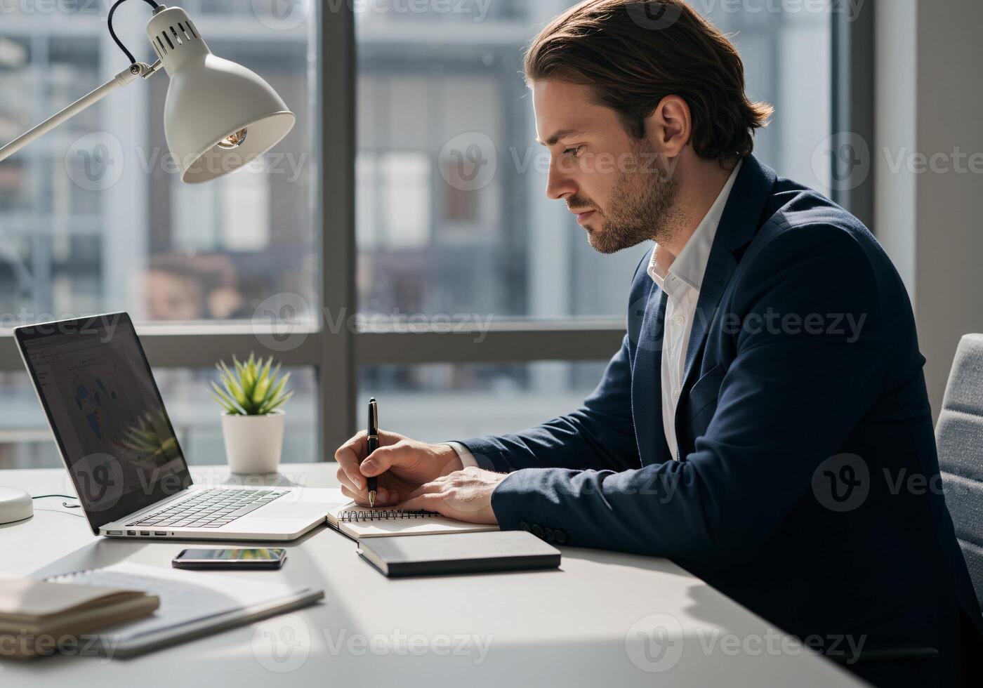 Focused Businessman Working on Laptop and Writing in Notebook photo