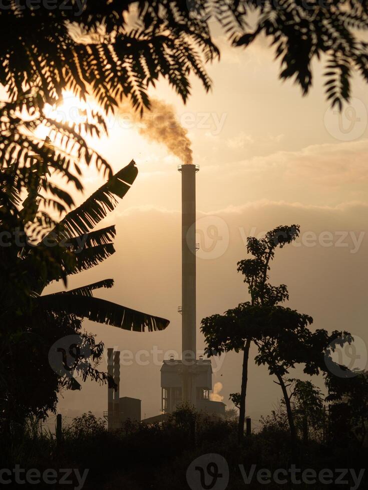 Smoke coming out of factory chimneys causes air pollution that contaminates the environment. Industrial waste is hazardous to public health. A chimney with evening and sunset view. photo