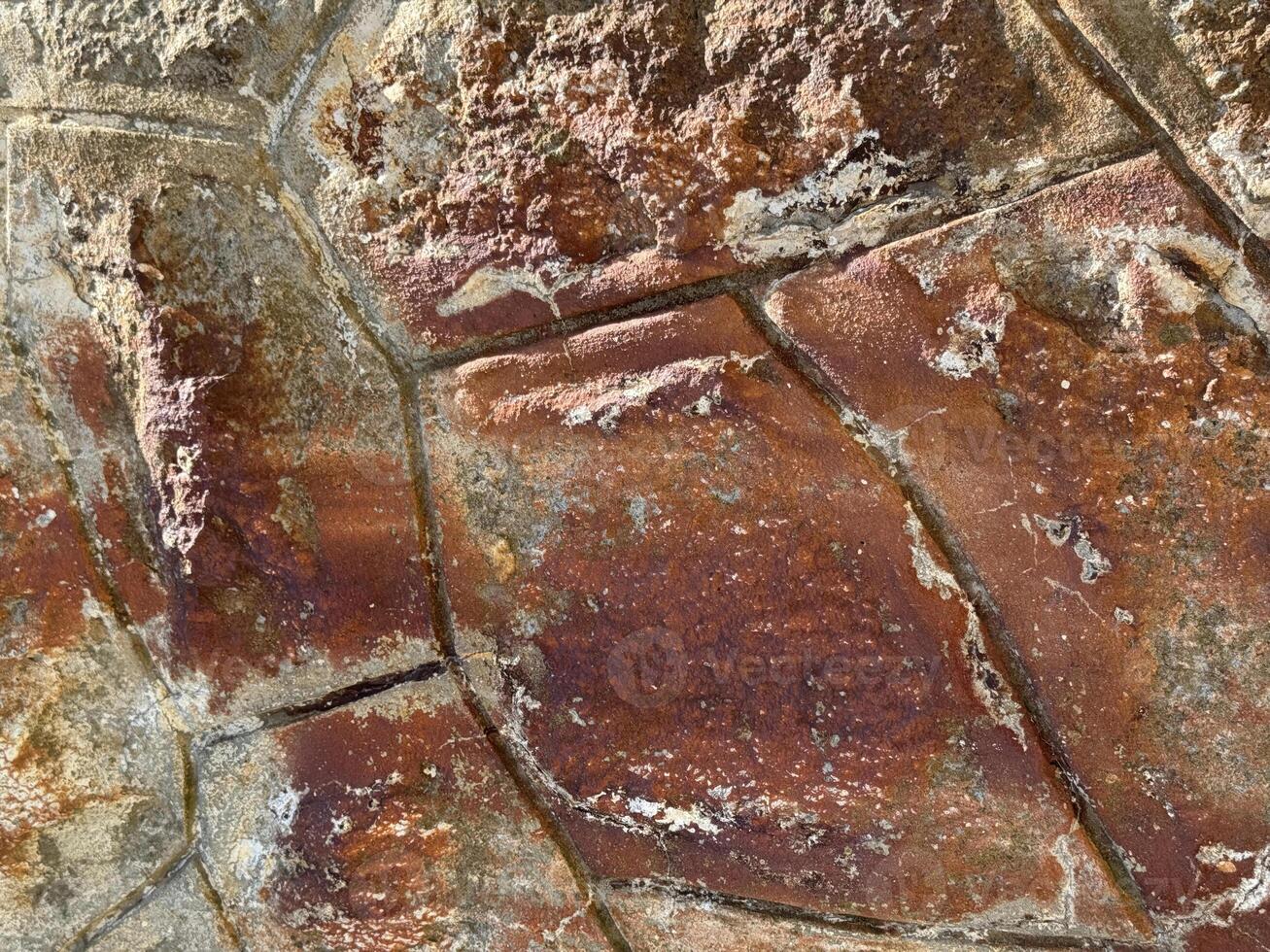 Close-up of a weathered red stone surface with cracks, rust stains, and textured erosion, evoking vintage architecture and raw urban atmosphere photo