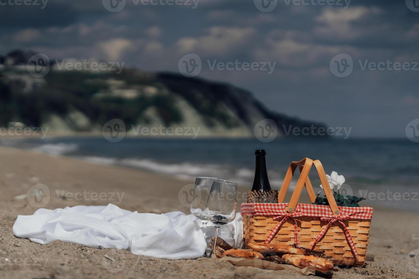 Elegant beach picnic with wine glasses and food by the sea under cloudy sky photo