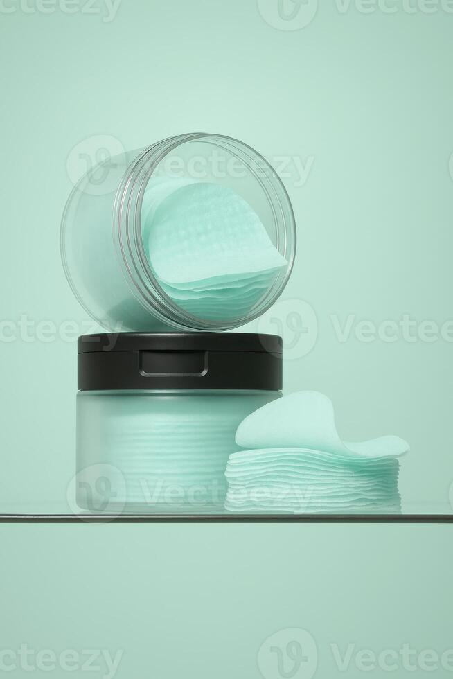 Minimalist close-up of two transparent jars filled with mint-colored skincare toner pads, placed on a glass surface with matching mint green background. photo